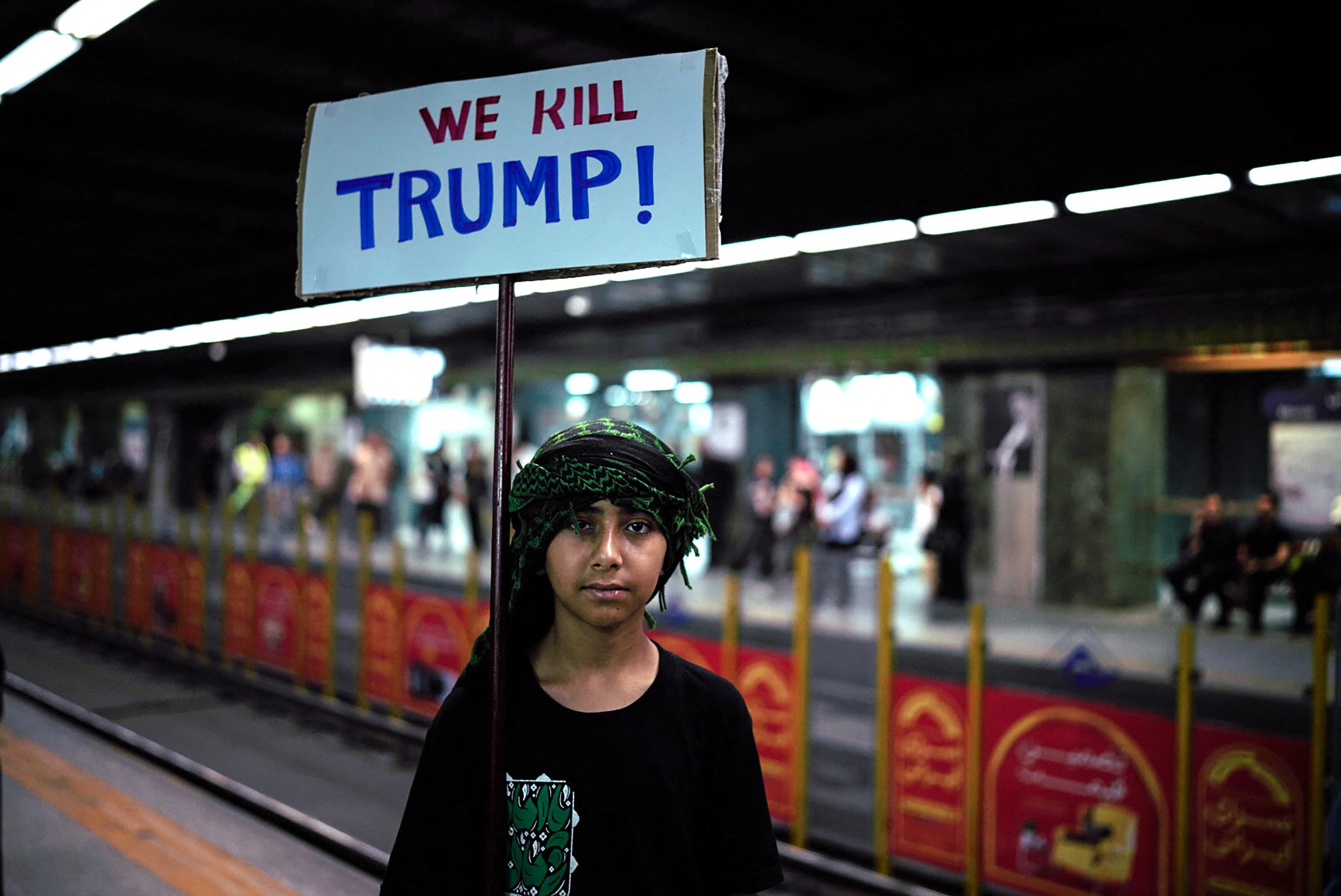 เด็กคนหนึ่งโพสท่าถ่ายรูปโดยถือป้ายต่อต้านประธานาธิบดี โดนัลด์ ทรัมป์ ของสหรัฐฯ ขณะที่ผู้คนมารวมตัวกันก่อนขบวนแห่ศพของอาลี คาเมเนอี ผู้นำสูงสุดของอิหร่านที่ถูกสังหาร ก่อนจะนำไปฝังที่สุสานอิหม่ามเรซา สถานที่ศักดิ์สิทธิ์ที่สุดของอิหร่าน ในเมืองมาชาด เมื่อวันที่ 9 กรกฎาคม 2026 Photo by - / AFP
